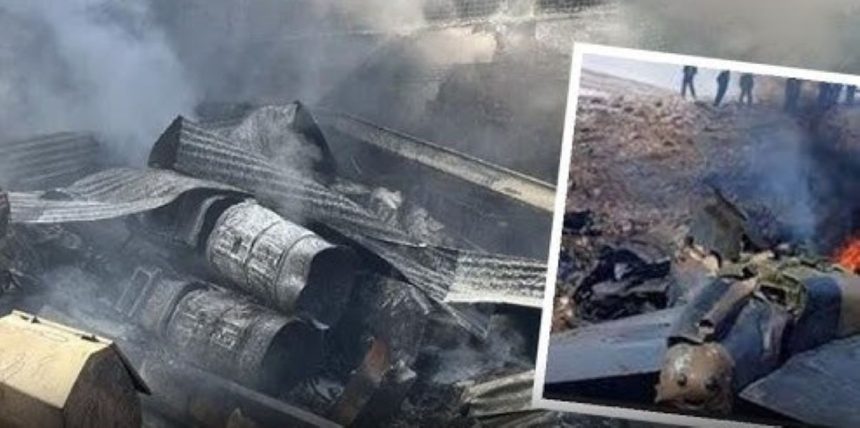 Wreckage from Iranian Army helicopter crash in Isfahan showing twisted metal debris, oil drums, and damaged fuselage amid smoke.