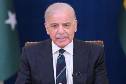 Prime Minister Shehbaz Sharif sits at a desk during an official address, with the Pakistan flag behind him.