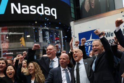 Group of people cheering with raised fists and confetti beneath a large Nasdaq sign.
