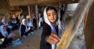 A schoolgirl in a white headscarf stands in a classroom at Batash School in Faizabad, Afghanistan, while other girls sit behind her.