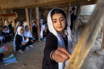 A schoolgirl in a white headscarf stands in a classroom at Batash School in Faizabad, Afghanistan, while other girls sit behind her.