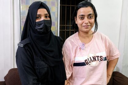 Anmol Pinky stands indoors beside a female police official wearing a black uniform, head covering, and face mask.