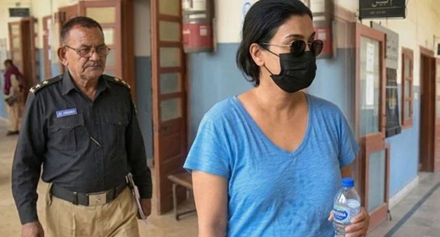 Anmol Pinky walks through a courthouse hallway wearing sunglasses and a black face mask, while a police officer follows behind her.