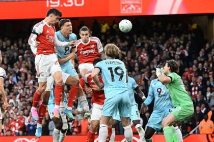 Arsenal players in red and white kits jump for a header against Burnley players in light blue during a football match.