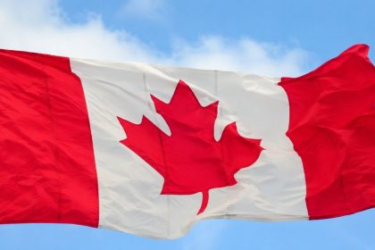 The Canadian flag waves in the wind against a blue sky.