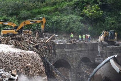 Construction crews and excavators remove mud, logs, and debris from a damaged bridge after flooding in China.