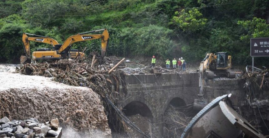 Construction crews and excavators remove mud, logs, and debris from a damaged bridge after flooding in China.