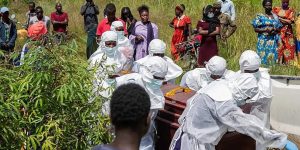 Health workers in white protective suits carry coffins as residents watch during an Ebola outbreak response in the Democratic Republic of Congo.