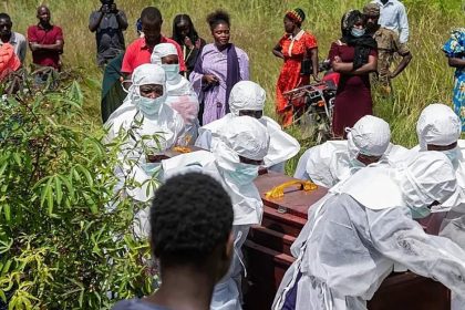 Health workers in white protective suits carry coffins as residents watch during an Ebola outbreak response in the Democratic Republic of Congo.