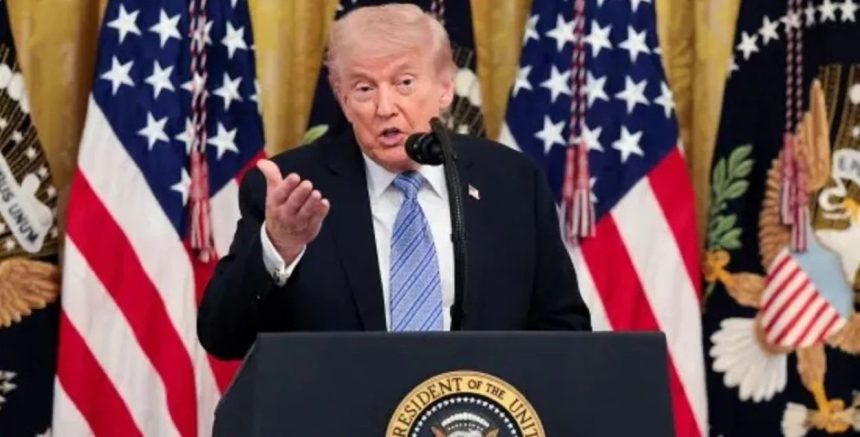 Donald Trump gestures while speaking at a podium in front of several U.S. flags.