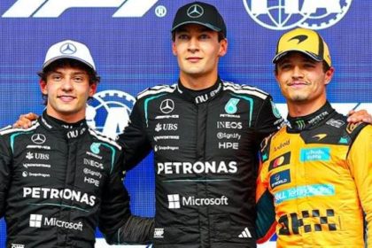 George Russell, Kimi Antonelli and Lando Norris stand side by side in Formula 1 racing suits.