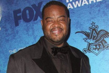 Grizz Chapman smiles while posing in a black suit and bow tie at an awards event.