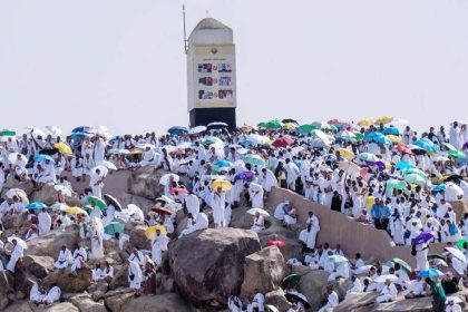 Large crowds of Hajj pilgrims in white garments gather with umbrellas on the rocky plains of Arafat.