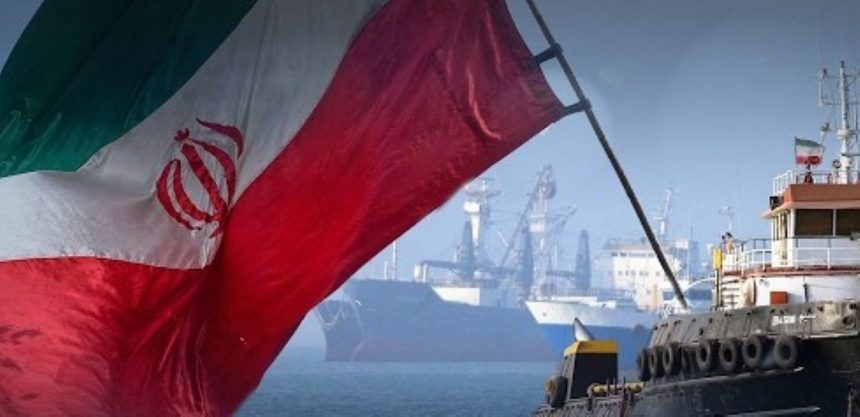 Iranian flag waving in front of ships and port cranes near a waterfront.