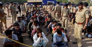Police officers supervise groups of detained people seated on the ground near a holding centre in West Bengal.