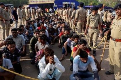 Police officers supervise groups of detained people seated on the ground near a holding centre in West Bengal.