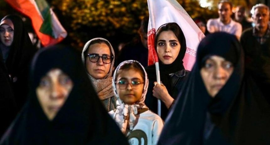 A nighttime crowd scene shows women and other attendees in Tehran, with one young woman holding an Iranian flag during a public rally in support of the government and armed forces.