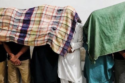 Suspects arrested by Karachi Police in a kidnapping case stand against a wall with cloths covering their faces.