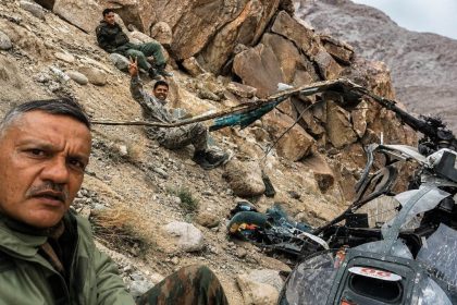 Indian Army personnel sit on a rocky mountainside near damaged helicopter wreckage after a crash in Leh.