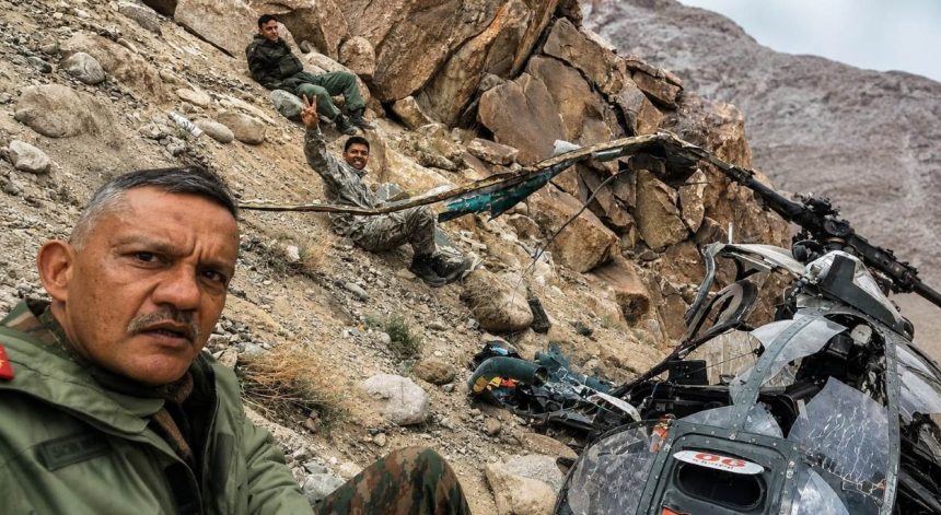 Indian Army personnel sit on a rocky mountainside near damaged helicopter wreckage after a crash in Leh.