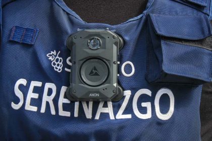A close-up shows an Axon body camera attached to a blue Serenazgo vest worn by a municipal security officer.