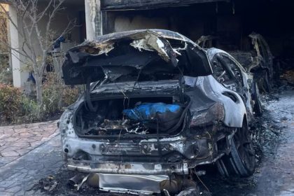 A severely burned car sits in a driveway outside a fire-damaged building following a reported arson incident in Melbourne.
