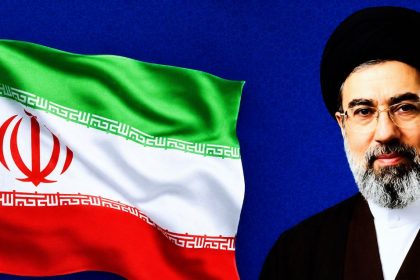 Iran’s Supreme Leader Mojtaba Khamenei appears beside a waving Iranian flag against a blue background.
