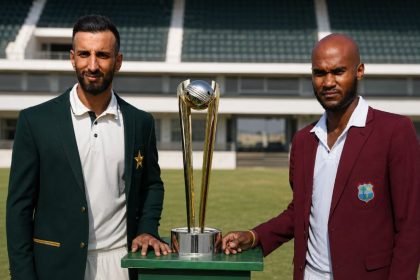 Shan Masood and Roston Chase standing with a cricket trophy at a stadium.