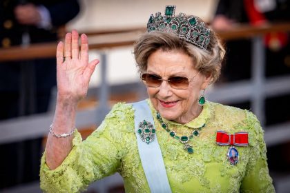 Queen Sonja of Norway waving in a green lace dress and tiara at a royal celebration.