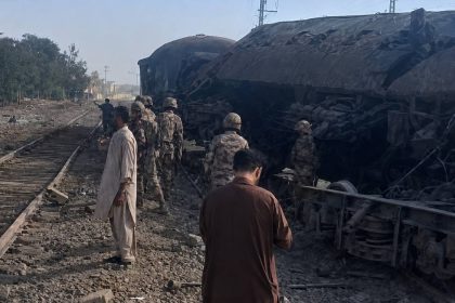 Security personnel and civilians stand beside damaged railcars and train tracks after a blast near Chaman Phatak in Quetta.