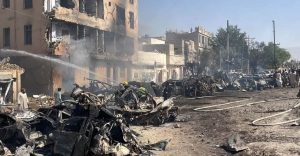 Burned vehicles, damaged buildings, smoke and fire hoses are visible after an explosion near Chaman Phatak in Quetta.