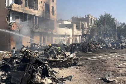 Burned vehicles, damaged buildings, smoke and fire hoses are visible after an explosion near Chaman Phatak in Quetta.