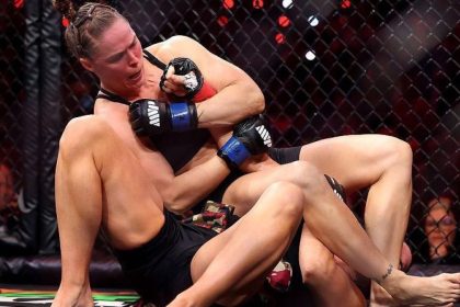 Ronda Rousey applies an armbar submission during an MMA fight inside a cage.