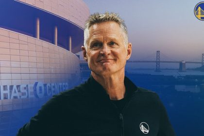 Golden State Warriors head coach Steve Kerr stands in front of a Chase Center and San Francisco Bay backdrop with the Warriors logo.