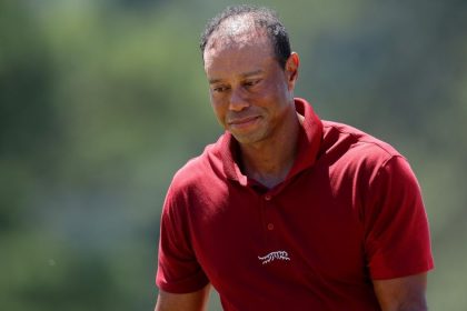 Tiger Woods wearing a red polo shirt on a blurred green golf course background. Image Credit: Getty Images