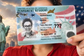 A person holds a U.S. permanent resident card in front of the Statue of Liberty and an American flag.