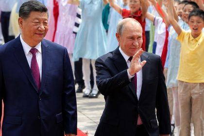 Chinese President Xi Jinping and Russian President Vladimir Putin walk on a red carpet as children wave flags during an official ceremony.