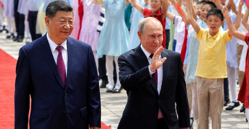 Chinese President Xi Jinping and Russian President Vladimir Putin walk on a red carpet as children wave flags during an official ceremony.
