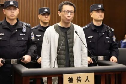 Xu Yao stands at a courtroom podium during a sentencing hearing, with police officers positioned behind him.