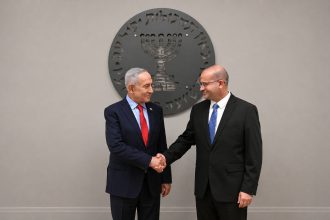 Israeli Prime Minister Benjamin Netanyahu shakes hands with Maj. Gen. Roman Gofman in front of an official emblem.