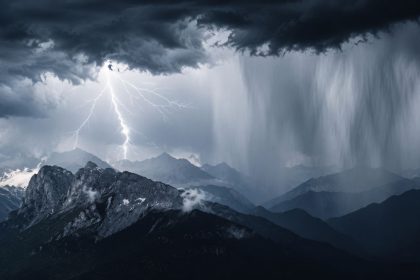 Lightning over dark mountain peaks during a severe storm with heavy rain and cloudburst conditions.