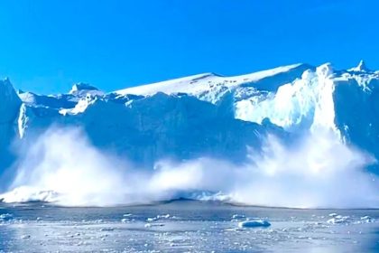 A massive Greenland iceberg collapses into the water, creating a large glacier wave and spray.