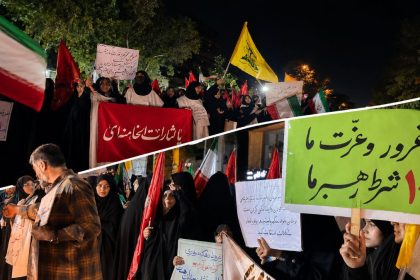Protest outside a foreign ministry office in Mashhad, Iran, with demonstrators holding Iranian flags, red banners and Persian-language signs.