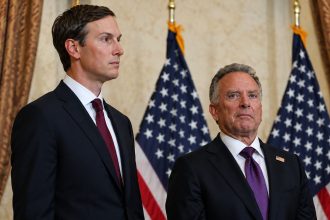 Senior adviser Jared Kushner and U.S. Special Envoy Steve Witkoff standing in suits in front of American flags.