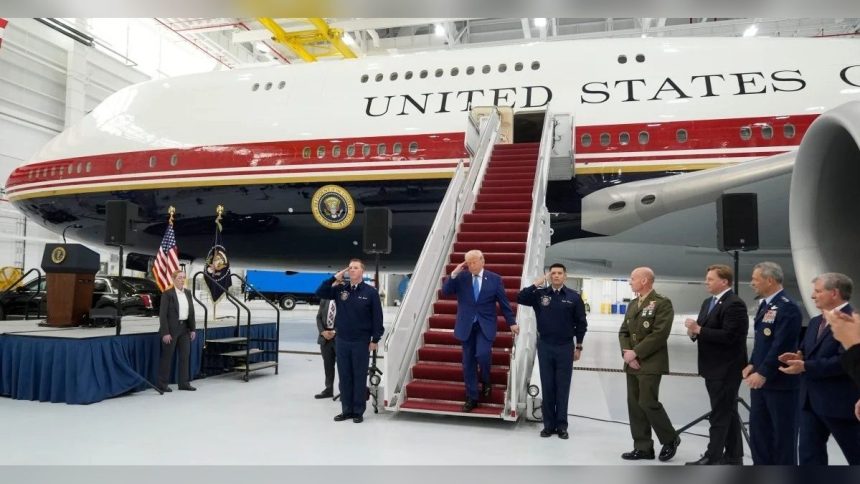 Donald Trump walks down red-carpeted aircraft stairs beside a large United States government plane inside a hangar.