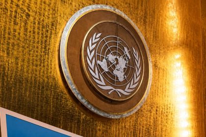 United Nations emblem displayed on a gold wall inside the UN General Assembly Hall.