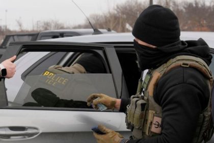 ICE officers beside a law-enforcement vehicle.