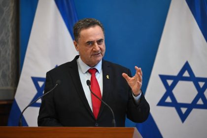 Israeli Defence Minister Israel Katz speaking at press conference with Israeli flags in background.