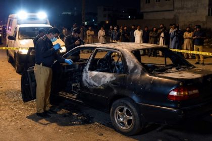 Karachi Police and forensic investigators examine the burned car near Zero Point in Shah Beg Goth, Surjani Town, during an ongoing investigation.