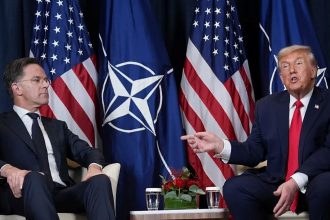 Mark Rutte and Donald Trump sit in front of NATO and US flags